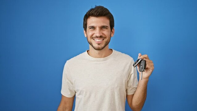 Smiling young man holding car keys against a blue background outdoors, portraying independence and ownership.