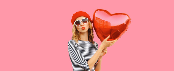 Sweet portrait of beautiful happy woman with red heart shaped balloon blows kiss - obrazy, fototapety, plakaty