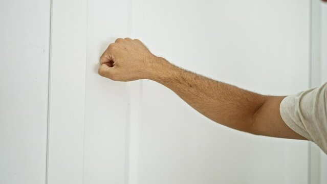 Close-up of a male hand knocking on a white door inside a bright home.