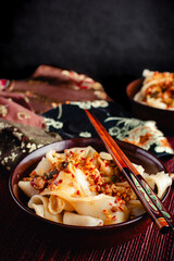 Biang Biang Noodles Topped with Spicy Chili Oil Sauce Close-up: Biang biang mian topped with minced pork and chili oil served in bowls with chopsticks