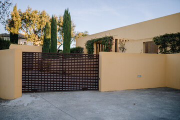 Slatted gate, yellow walls, driveway, cypress trees, flowering vines, clear sky...