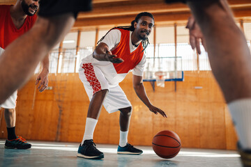 Interracial basketball player is dribbling ball while practicing with team.