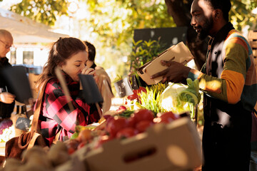 Happy girl smelling various eco apples at organic grocery stand with african american seller,...