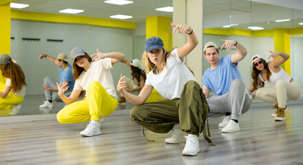 Group of young cool active dancers training together during dance rehearsal in spacious dance room