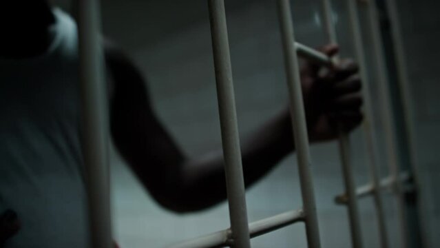 Close up shot of African American inmate standing behind bars of prison cell and getting mobile phone from corrupt guard
