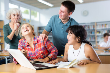 Mature European teacher woman asks amused schoolchildren to behave a little quieter, who are preparing for classes in the school library