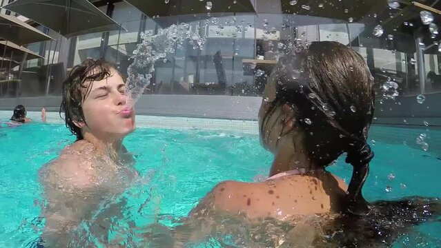 Boy and girl spit to each other in swimming pool near cafe and hotel