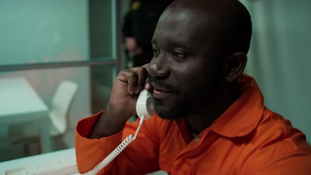 Positive African American inmate having phone conversation with family and smiling while having meeting in prison