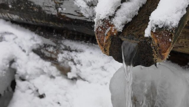 Water stream runs from wooden gutter at winter day. 