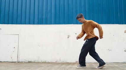 Hispanic man stretch arms and dance street dancing in front of wall. Motion shot of stylish dancer or choreographer in casual outfit practicing dancing in hip hop style. Outdoor sport 2024. Endeavor.