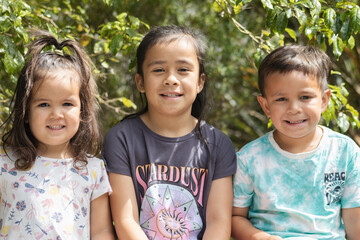 a close up image of three maori children sitting for their family portrait outdoors in a natural setting.