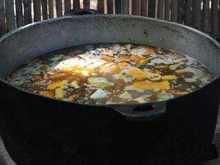 Big iron pot on fire cooking soup, sancocho Dominican meat and vegetables stew.
