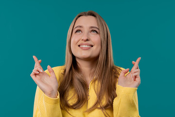 Young woman praying with crossed fingers on blue background. Lady begs someone