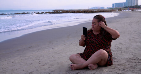 Woman sitting on the beaches of Cartagena de Indias looking at her mobile phone and fixing her hair.