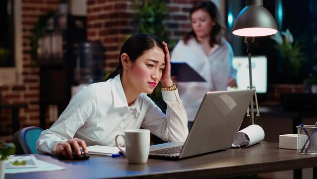 Asian employee gasping, shocked by negative response received from customer while discussing business matters over email. Worker wincing while looking at laptop screen, feeling disappointed