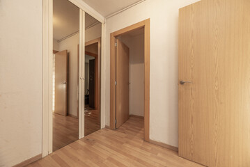 Small hall of a home with light floors, built-in wardrobe with mirrors and imitation oak wood doors leading to several rooms