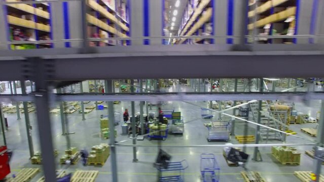 Many shelves with goods and conveyer in Ozon company storage hangar with workers. Aerial view