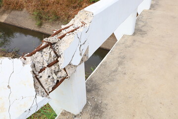 Broken concrete bridge railing. Closeup of the edge of a white cement bridge over an irrigation canal that has cracked due to an accident can be dangerous for users. Selective focus