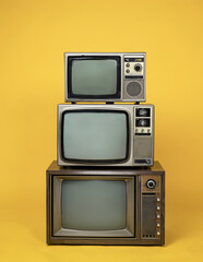 Antique retro old televisions pile on yellow floor. Vintage style. Three old TVs isolated over yellow background.