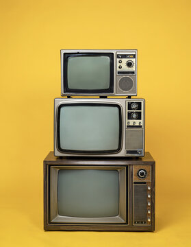 Antique retro old televisions pile on yellow floor. Vintage style. Three old TVs isolated over yellow background.