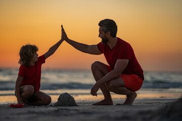 Kid and father building sandcastle. Father and son playing on beach. Friendly family. Father and...