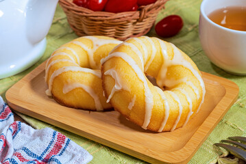 Donut with white icing on wooden plate on wooden table background.  
