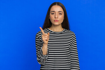 Fototapeta premium Quarrel. Displeased young woman gesturing hands with irritation and displeasure, blaming scolding for failure, asking why this happened. Brunette attractive girl isolated on blue studio background