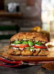 A delectable mozzarella sandwich featuring fresh basil, ripe tomatoes, pesto, and mayonnaise artfully arranged on a wooden cutting board, set against a rustic cabin backdrop