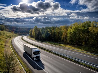 White truck driving on the highway winding through forested landscape in autumn colors at sunset...