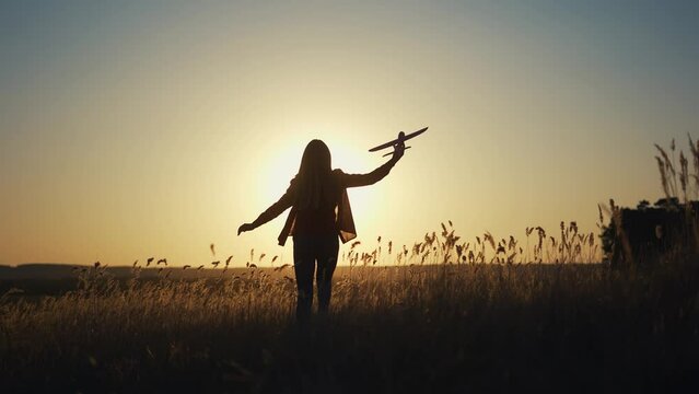 girl runs across the field. concept of a happy childhood and loving family. girl runs across a field with an airplane in her hands, silhouette of a child, sunset on the background lifestyle