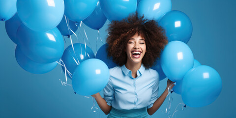 Cheerful curly haired woman dressed in blue clothes, laughing around inflated helium balloons over...
