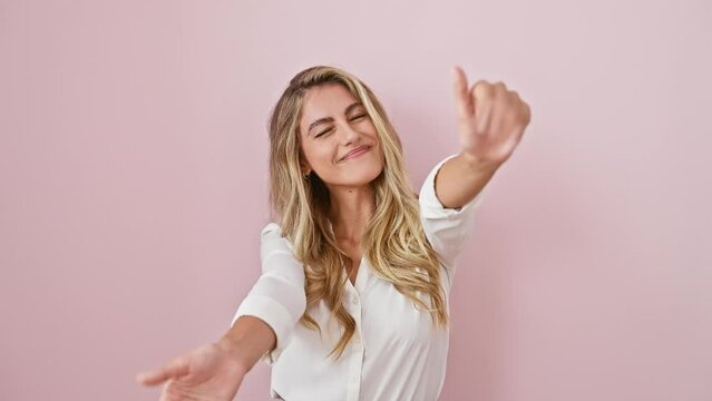 Joyful young blonde woman, standing over pink isolated background, arms wide open, wearing shirt, welcomes you with a cheerful smile and a hug ready to embrace happiness.