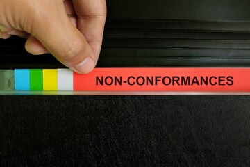 Nonconformances in audit findings concept. Human hand picking document in a folder binder.