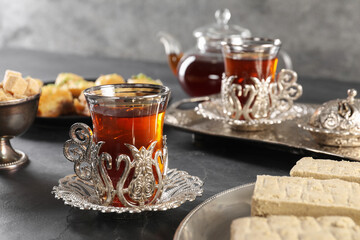 Turkish tea and sweets served in vintage tea set on black table, closeup