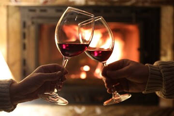 Couple clinking glasses of wine near fireplace at home, closeup