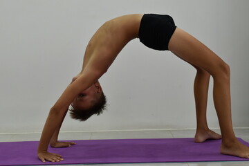Athlete boy in black shorts on a yoga mat stands in a pose.
