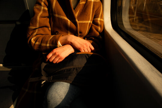 A young stylish woman in a brown checkered coat riding on her knees on a train, bus. A passenger seat in public transportation. Brown cinematic filter