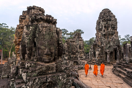 Three buddhist monks walking near giant Buddha face, Bayon temple, Angkor Wat, Cambodia