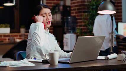 Company secretary taking phone call at office desk, answering customer inquiries while working on laptop, multitasking. Stressed worker having conversation on telephone and crosschecking data