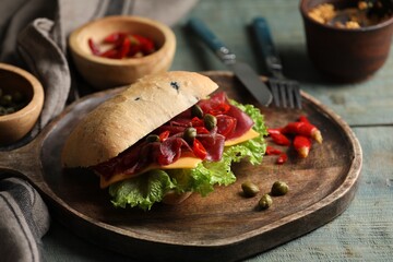 Delicious sandwich with bresaola, cheese and lettuce served on light blue wooden table, closeup