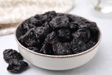 Bowl with sweet dried prunes on light table, closeup