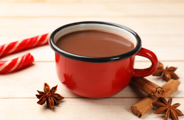 Tasty hot chocolate, candy cane and spices on light wooden table, closeup