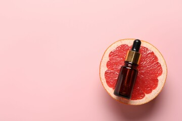 Bottle of grapefruit essential oil and fresh fruit on pink background, top view. Space for text