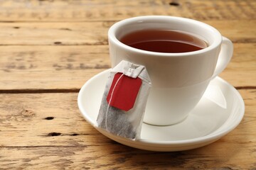 Tea bag and cup of hot beverage on wooden table, closeup. Space for text