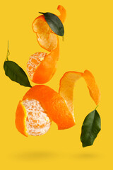 Flying sweet ripe mandarins and green leaves on yellow background
