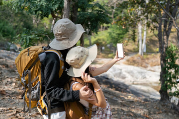 Happy LGBT Lesbian couple selfie with mobile while Hiking with Backpacks in forest Trail. LGBT Lesbian Couple Hikers with backpacks walks in mountains in vacation
