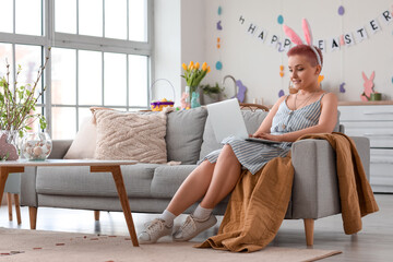 Young woman with bunny ears using laptop at home on Easter day