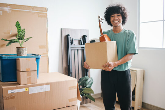 Happy Asian young man looking at camera while holding cardboard box moving in new house