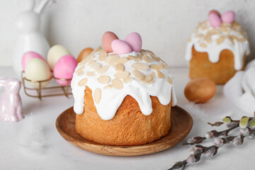 Easter cakes, painted eggs, bunnies and pussy willow branches on table near white wall