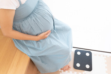 Pregnant woman sits down in front of weight scale